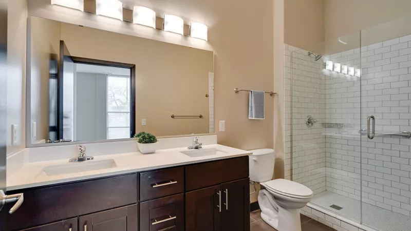 Clean bathroom with a dark wood double sink vanity, large mirror, toilet, and glass-enclosed shower with white subway tile.