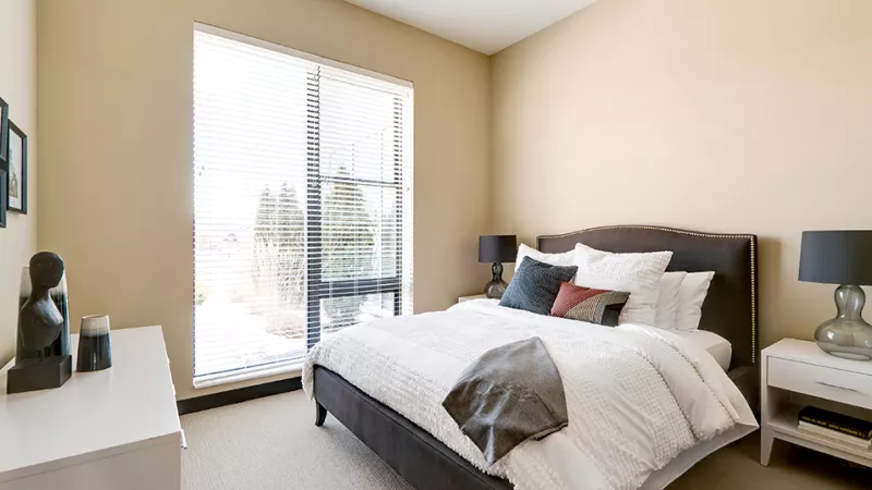 Modern bedroom with light beige walls, a large window, a bed with white bedding, and two nightstands.