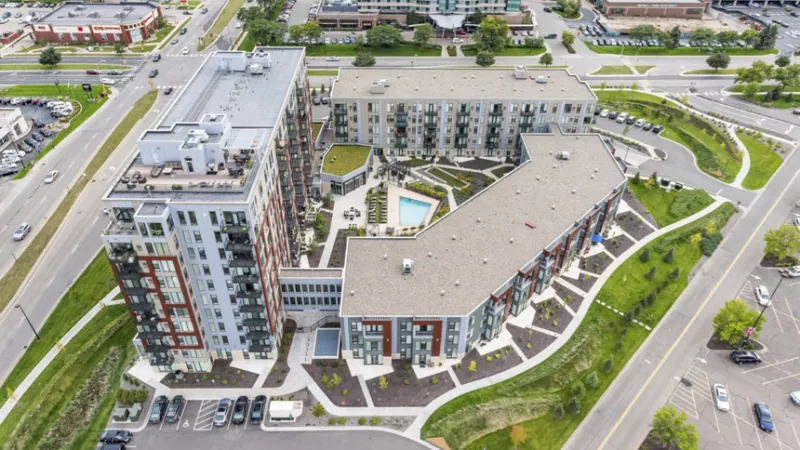Aerial photograph: Large modern apartment complex with multiple buildings, central courtyard, pool, and surrounding roads.