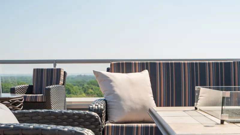 Rooftop patio with wicker chairs, striped sofa cushions, a light pillow, and a modern fire pit table.