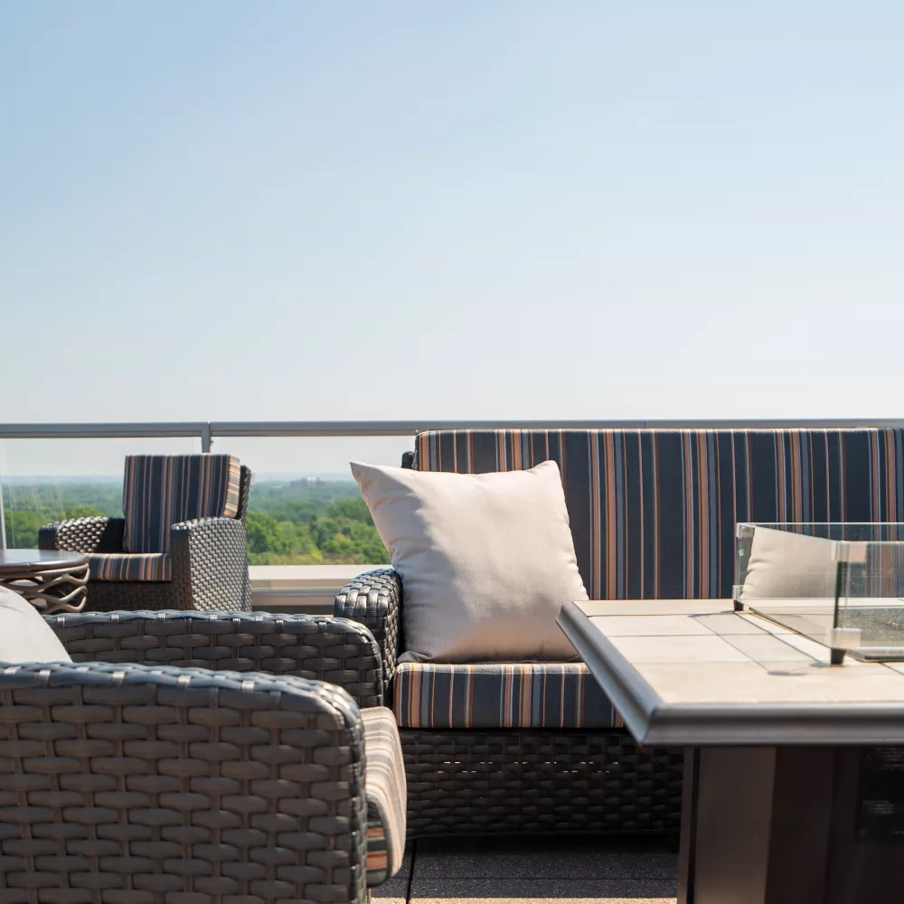 Rooftop patio with wicker chairs, striped sofa cushions, a light pillow, and a modern fire pit table.